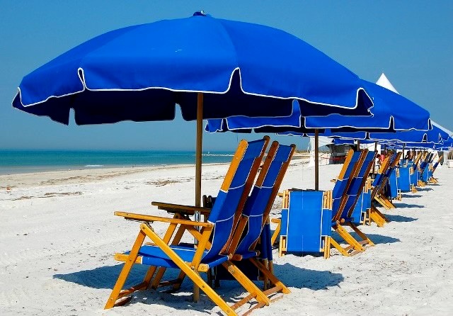 Beach with blue umbrellas and wooden lounge chairs lined up on the sand.