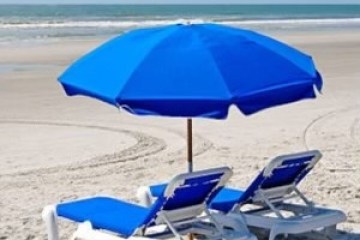 Two beach chairs under a blue umbrella on a sandy beach.
