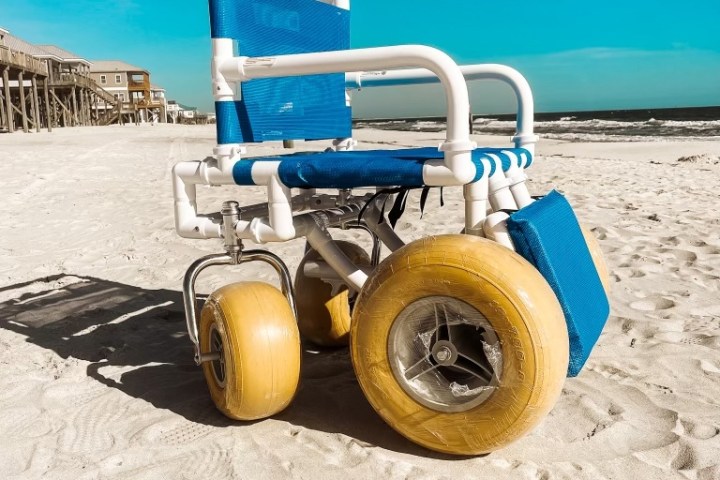 Beach wheelchair with large wheels on sandy shore under clear blue sky.