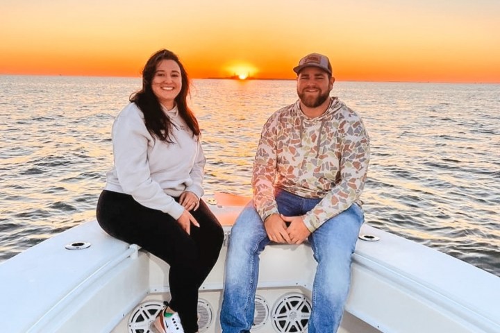 Two people sitting on a boat at sunset, smiling.