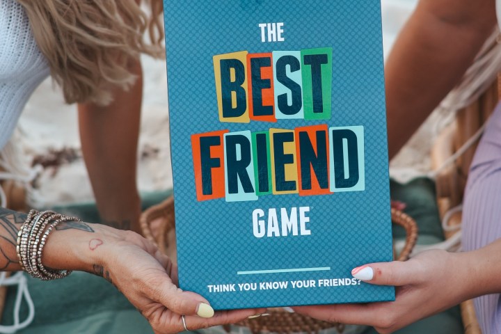 Two people holding 'The Best Friend Game' box on a picnic blanket.