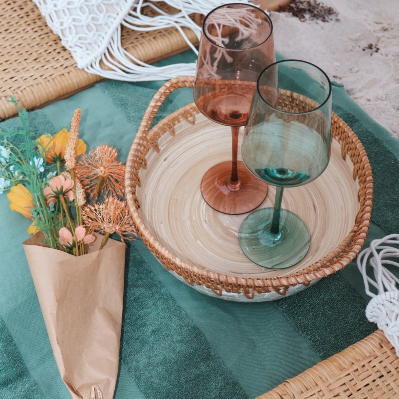 Two empty wine glasses on a basket with flowers on a picnic mat.
