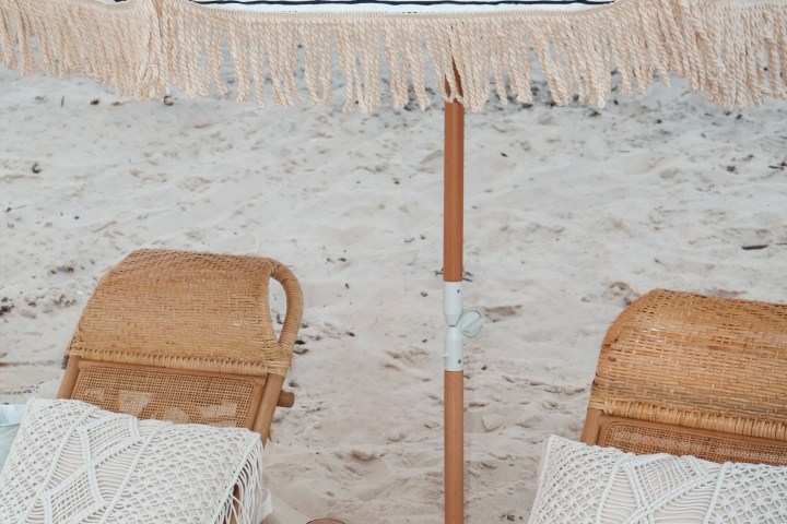 Two rattan chairs and umbrella on a sandy beach.