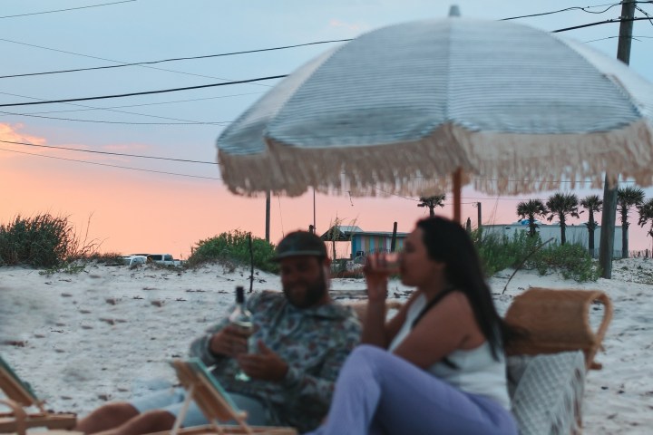Two people relaxing under a beach umbrella at sunset on a sandy beach.