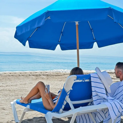 Two people relaxing under a blue umbrella on beach chairs by the sea.