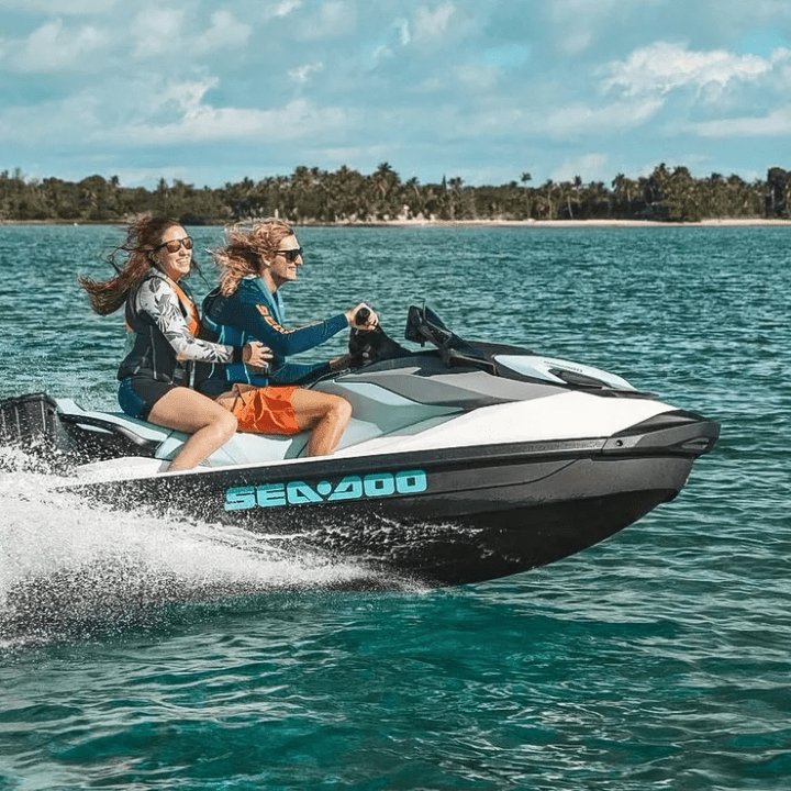 Two people riding a jet ski on the ocean near a tropical island.