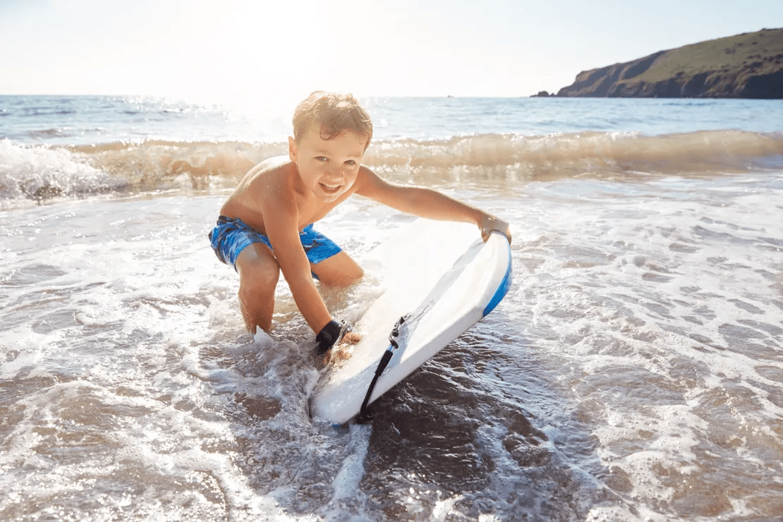 Child in blue shorts playing with a surfboard at the beach.