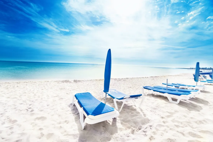Empty beach with blue sun loungers and umbrellas under a bright sky.