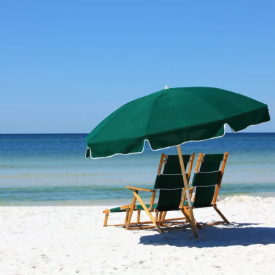 Two chairs and a green umbrella on a sandy beach by the sea under a clear blue sky.