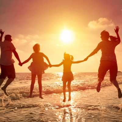 Family holding hands and jumping on a beach at sunset.